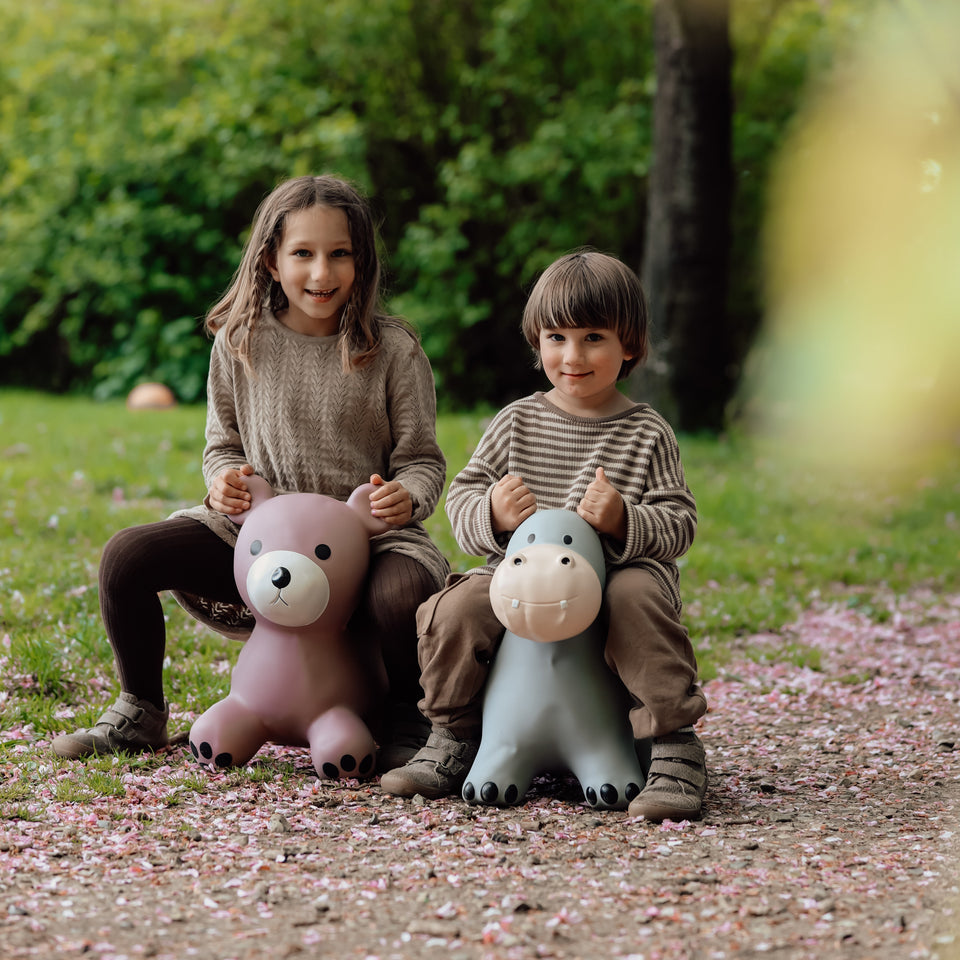 Two children sitting on inflatable animal toys in a park