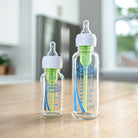Two Dr. Brown's baby bottles on a wooden surface with a blurred indoor background.