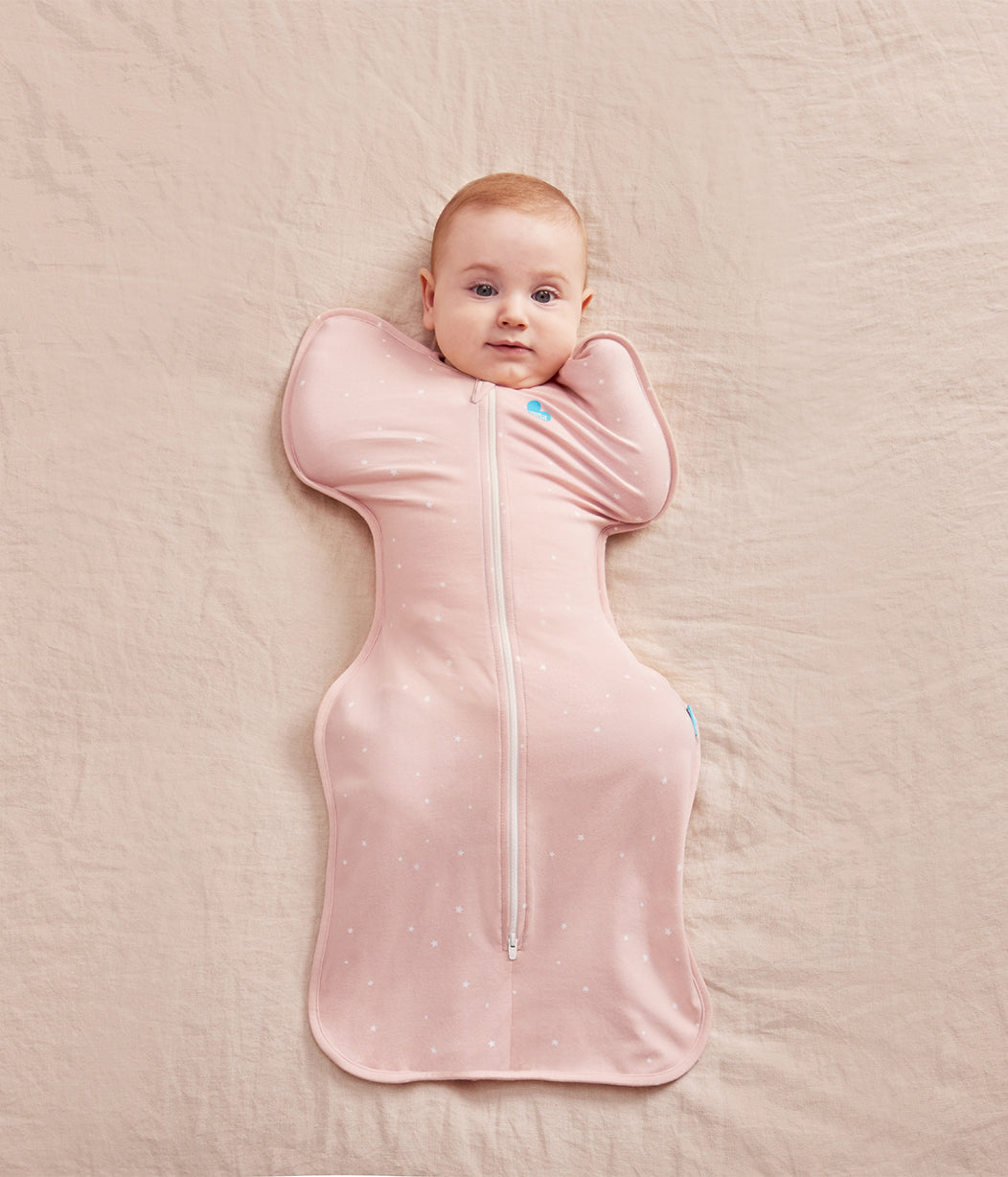 Baby lying on a pink blanket wearing a pink swaddle with a zipper.