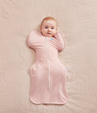 Baby lying on a pink blanket wearing a pink swaddle with a zipper.