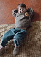 A young child wearing a muted checkered long-sleeve top paired with relaxed teal corduroy trousers.