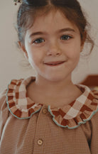 A young girl button-up shirt with a ruffled collar in brown, beige