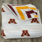 Folded blanket with red and yellow stripes and 'M' logos on a wooden surface