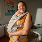 Woman smiling while holding a baby in a sling in a home setting