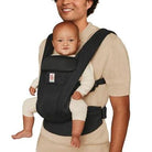 Person holding a baby in a black baby carrier on a white background