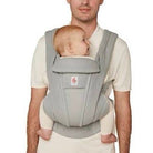 Person carrying a baby in a gray baby carrier.