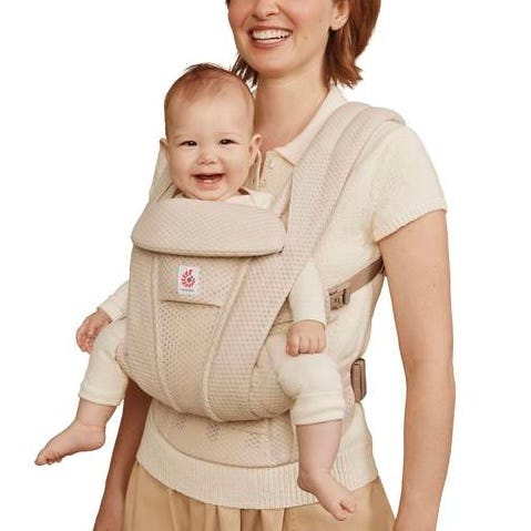 Woman carrying a baby in a beige baby carrier.