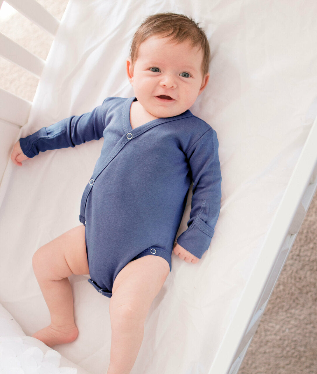 Baby wearing a blue onesie lying on a white crib