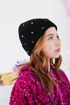 Person wearing a black beanie with colorful beads and a pink sequin jacket.