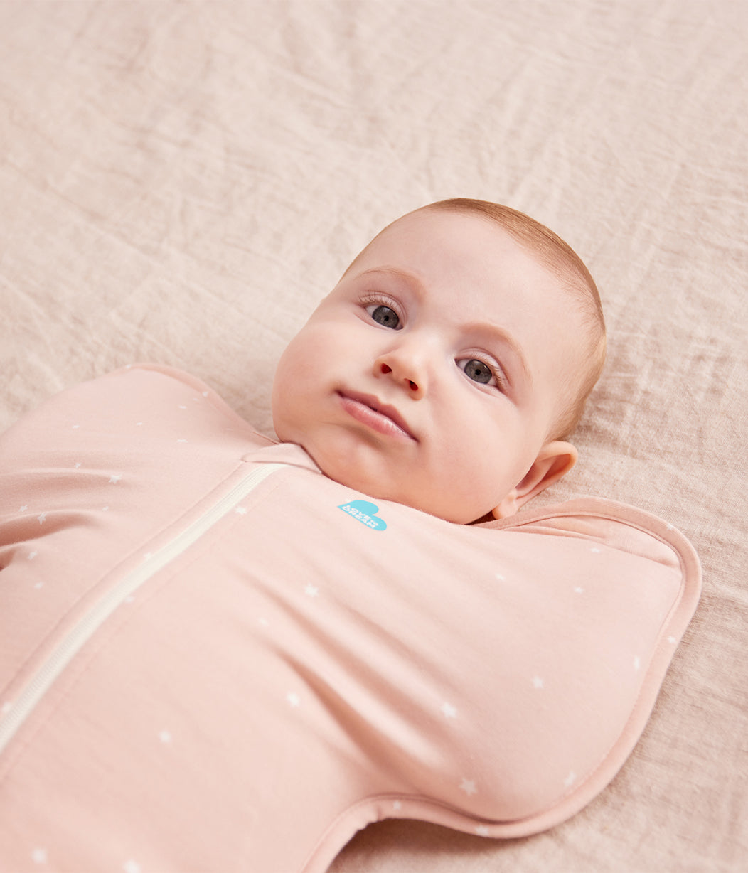 Baby wrapped in a pink swaddle on a soft beige blanket