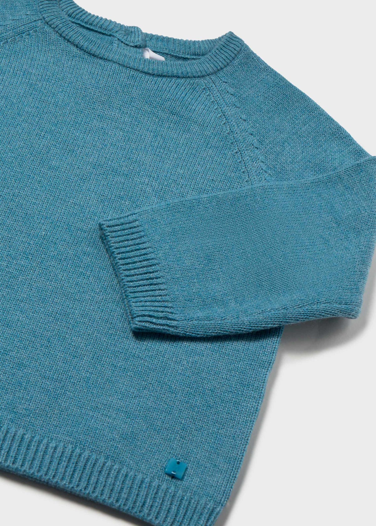 A close-up of a teal blue knit sweater with a crew neck and ribbed cuffs, laid flat on a light gray background.