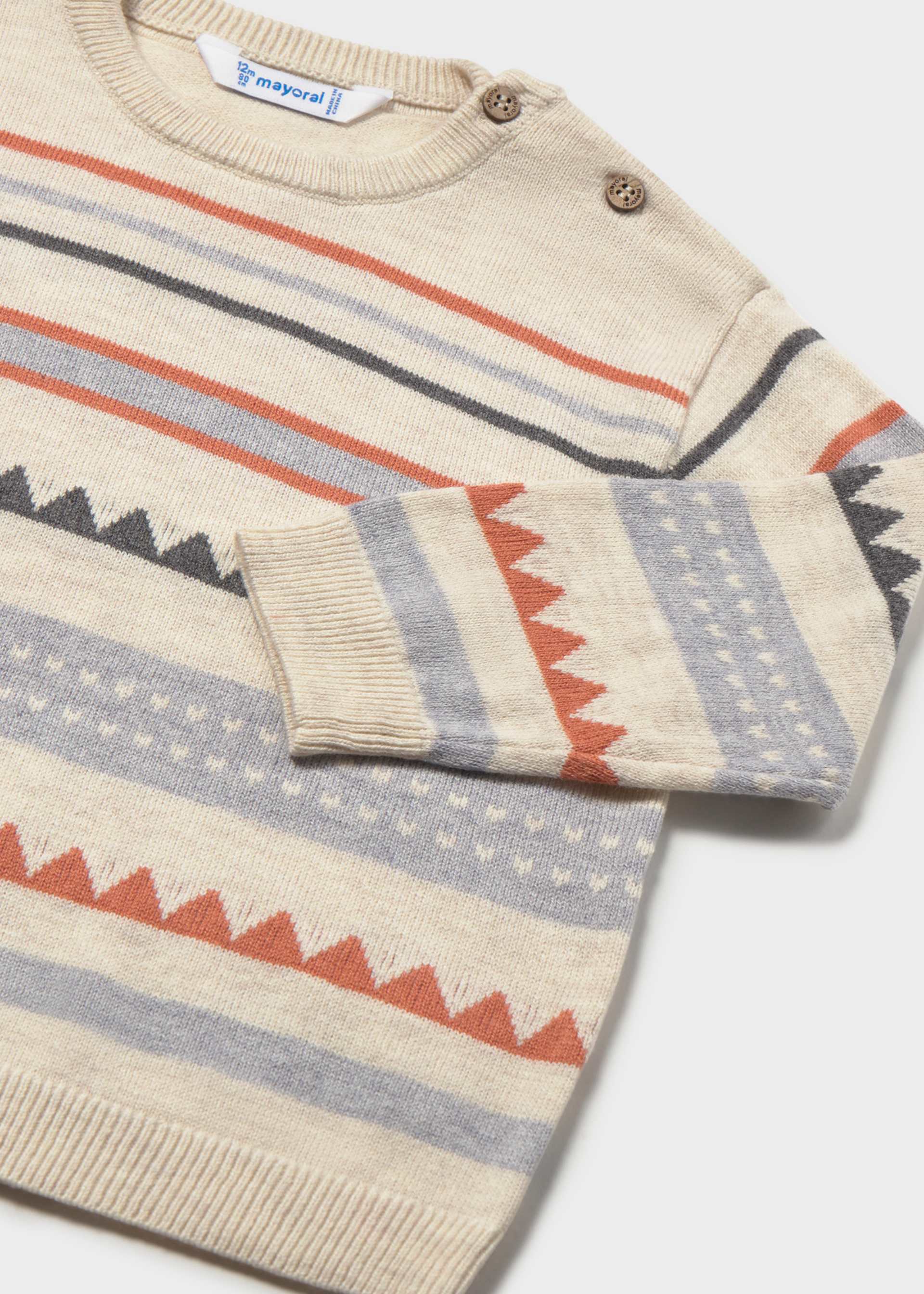Close-up of a Mayoral sweater featuring rust-orange sawtooth bands and shoulder button fastenings.