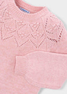 A close-up of a light pink knit sweater with a textured geometric lace pattern across the chest and a ribbed crew neck, sleeve, and cuffs. The brand label 'mayoral' is visible inside the collar.