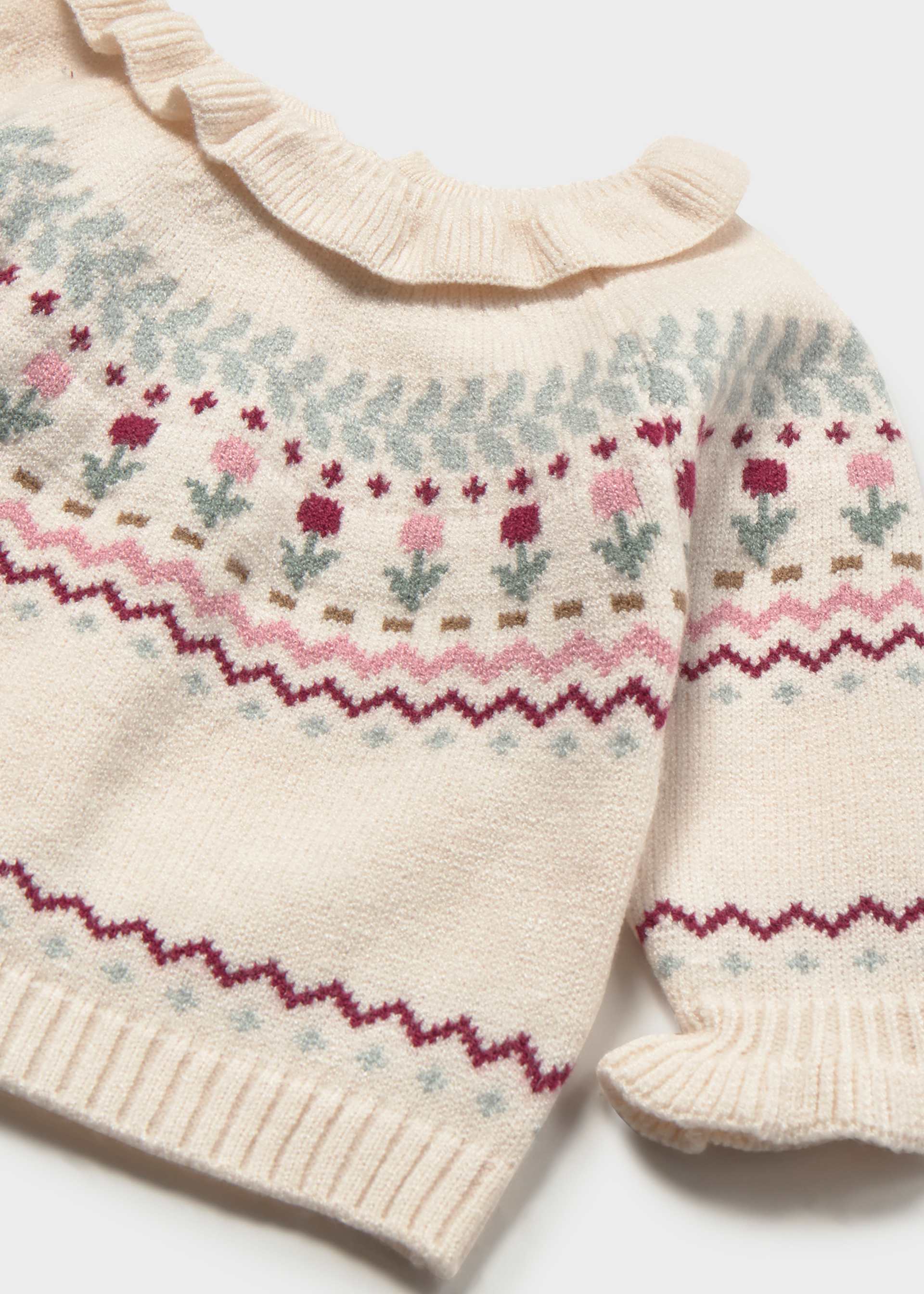 Close-up of a cream-colored knit baby sweater with a ruffled neckline and Fair Isle pattern featuring pink, burgundy, and light blue floral motifs.