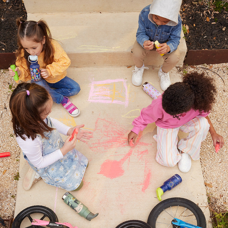 Four children playing with sidewalk chalk on a concrete surface.