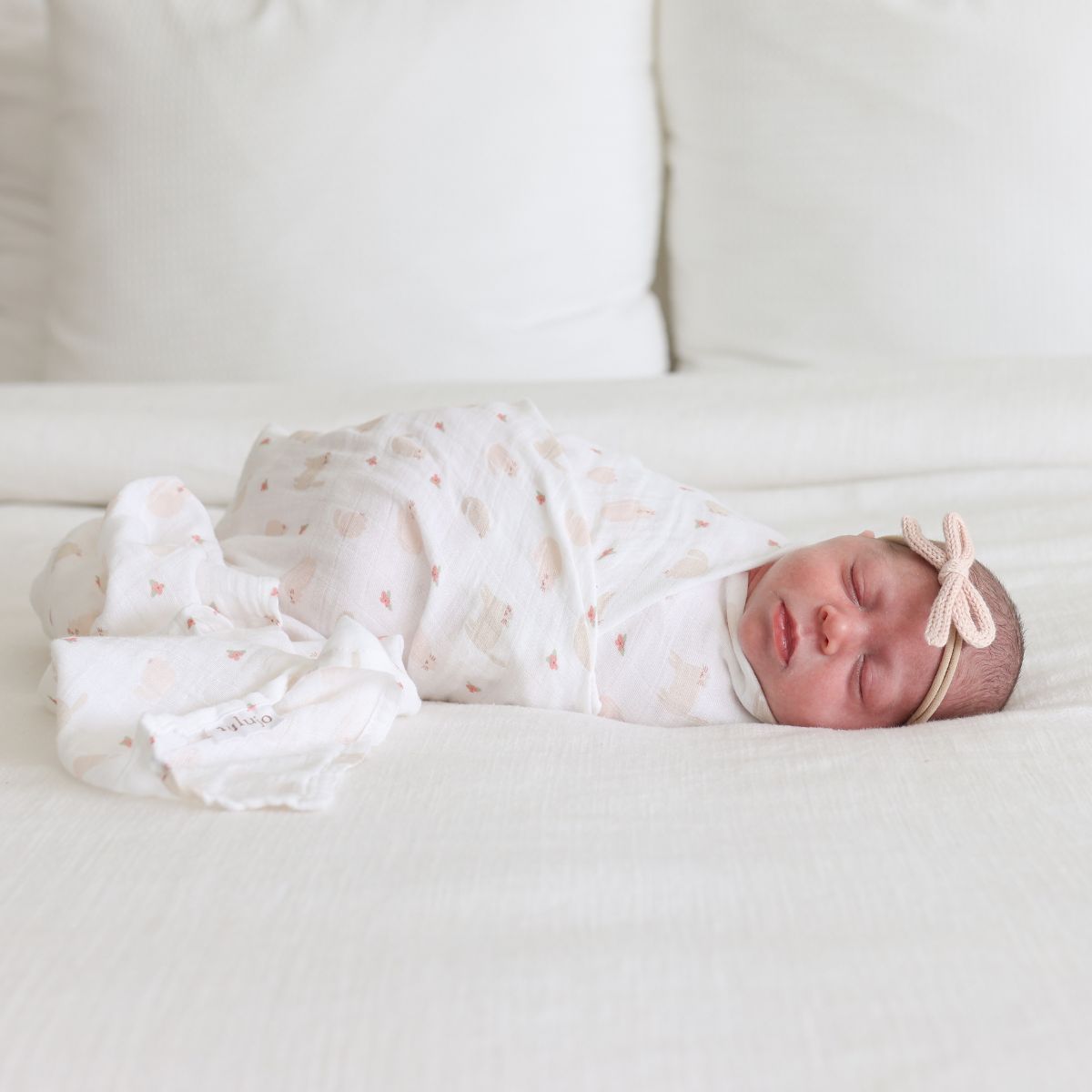 Newborn baby swaddled in a white blanket with pink details on a white couch.