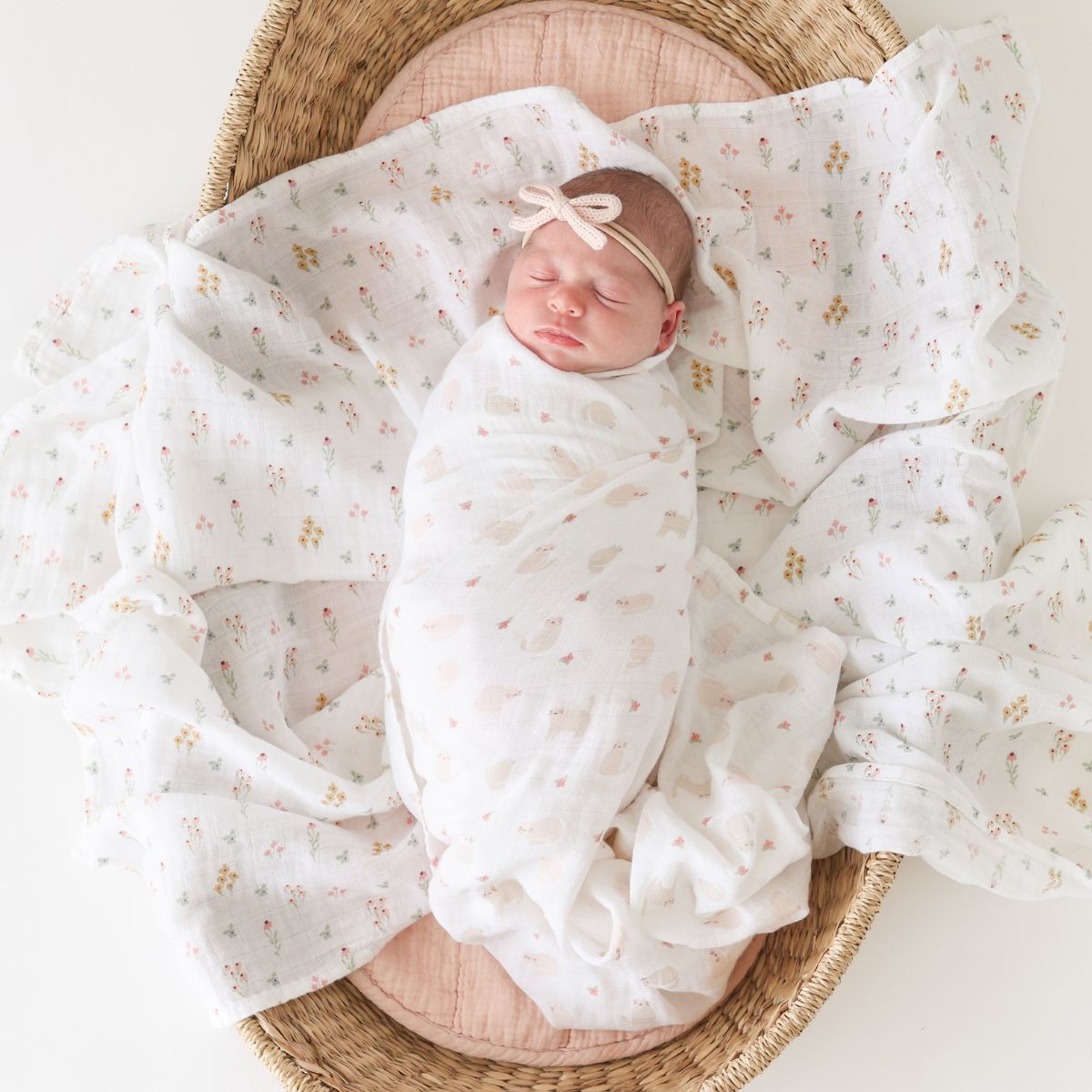 Newborn baby wrapped in a floral blanket inside a woven basket on a white background