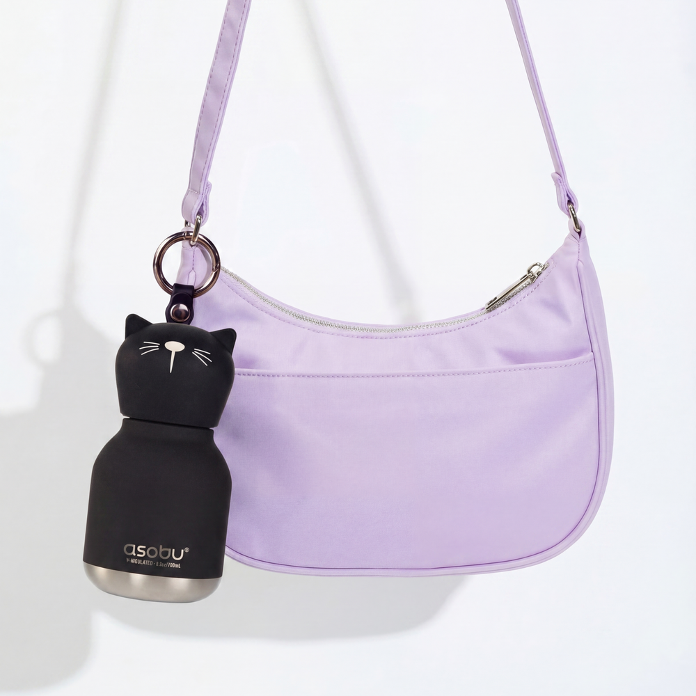 Black cat-shaped bottle with silver base next to a purple handbag on a white background