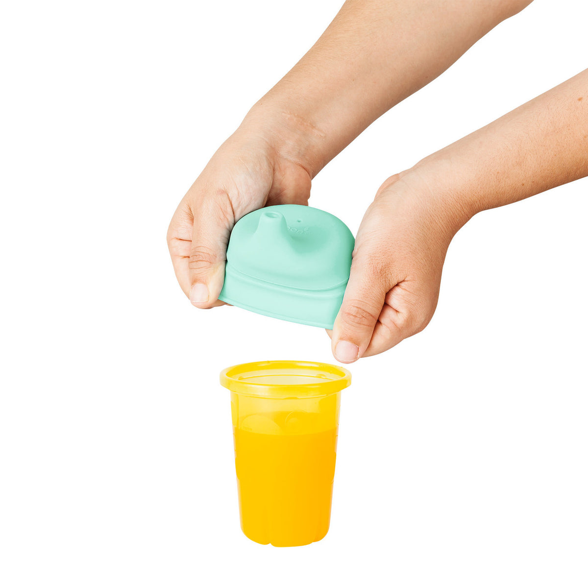 Child's hands using a green lid to open a yellow cup filled with orange juice on a white background