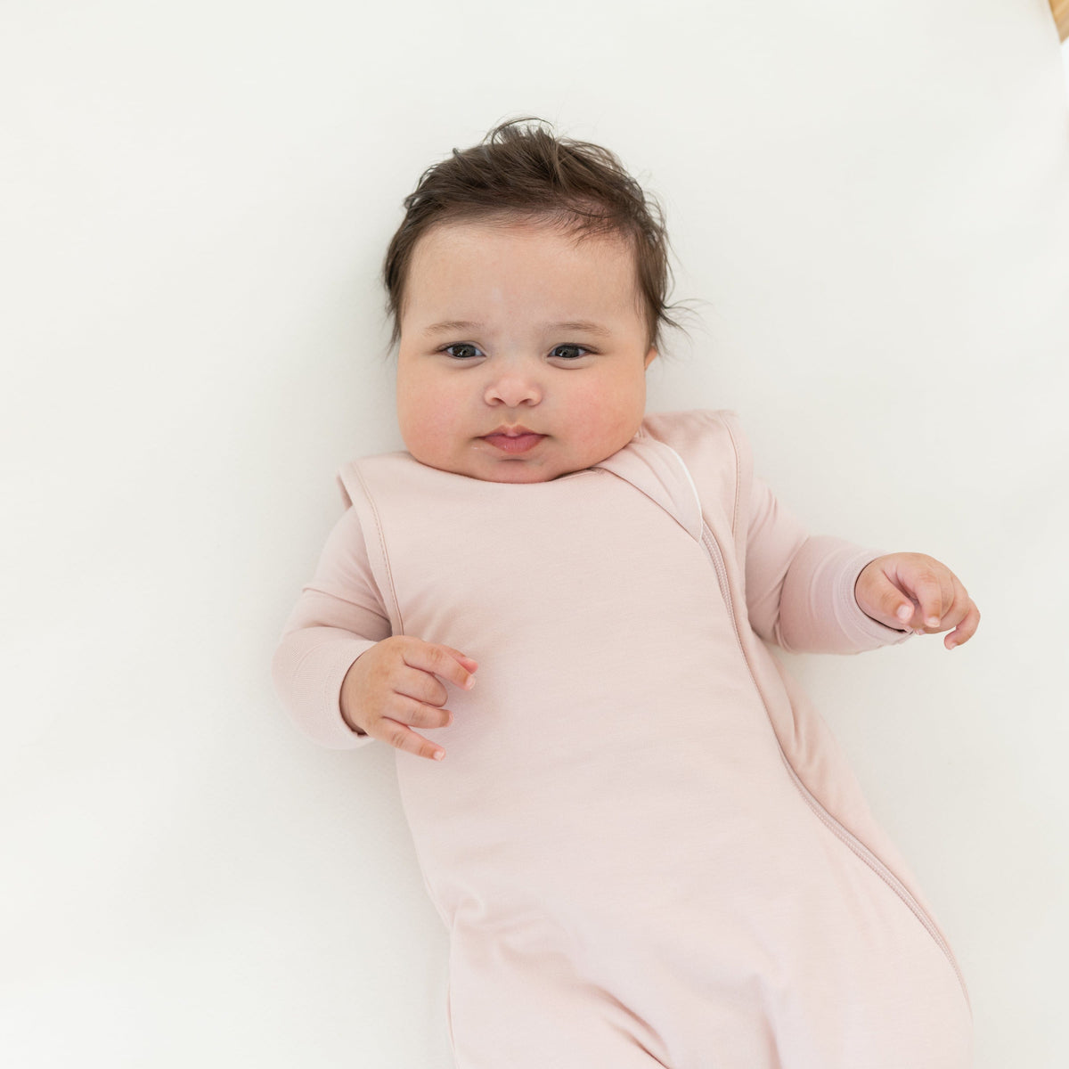 Baby in a pink onesie lying on a white surface