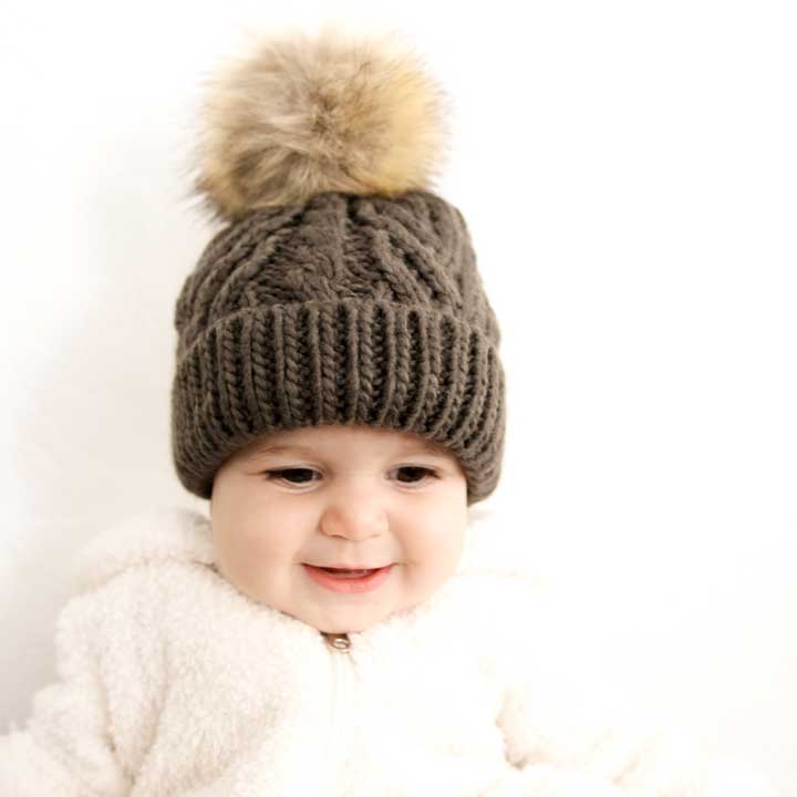 Child wearing a brown knitted hat with a pom-pom on a white background