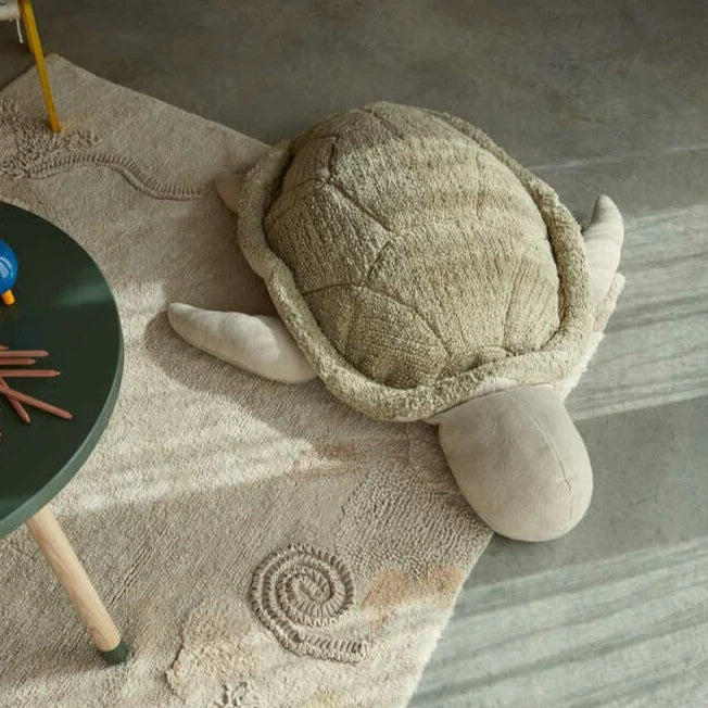 Plush turtle toy on a textured rug with a table and pencils in the background