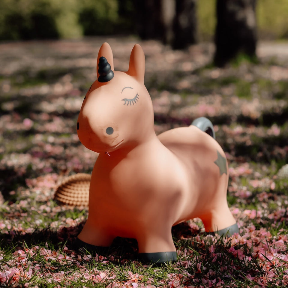 Unicorn-shaped toy on a grassy field with pink petals