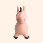A pink inflatable hippo-shaped toy with a black horn, black hooves, and simple black facial features, centered on a solid pale cream background.