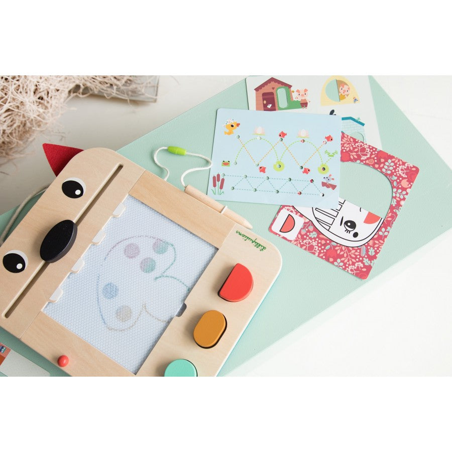 Children's drawing board with colorful shapes and a small book on a light green surface.