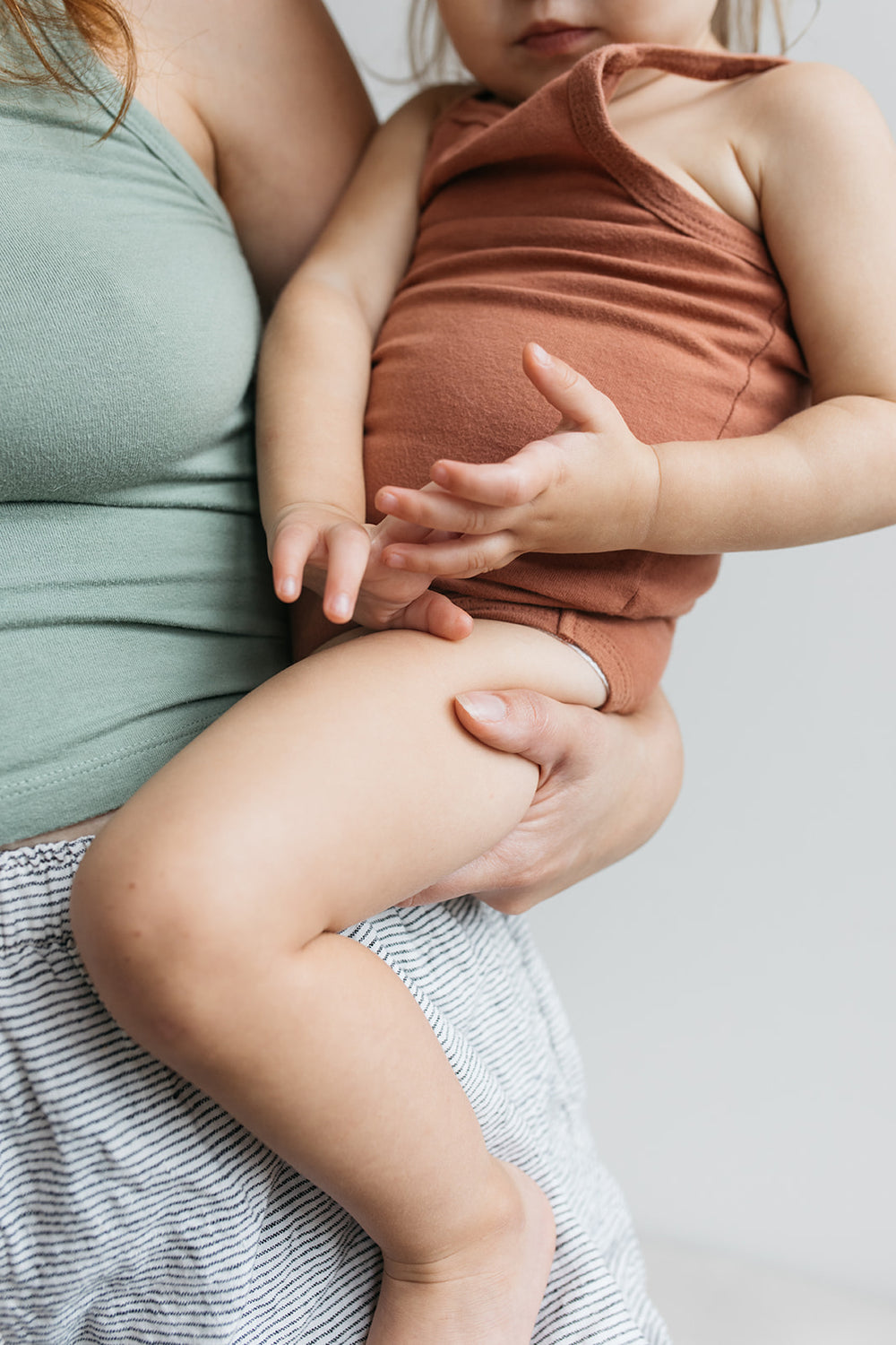 Close-up of a child in a rust-colored outfit being held by an adult against a neutral background