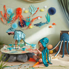 Children in ocean-themed costumes playing at a table with decorative sea creatures on the wall.