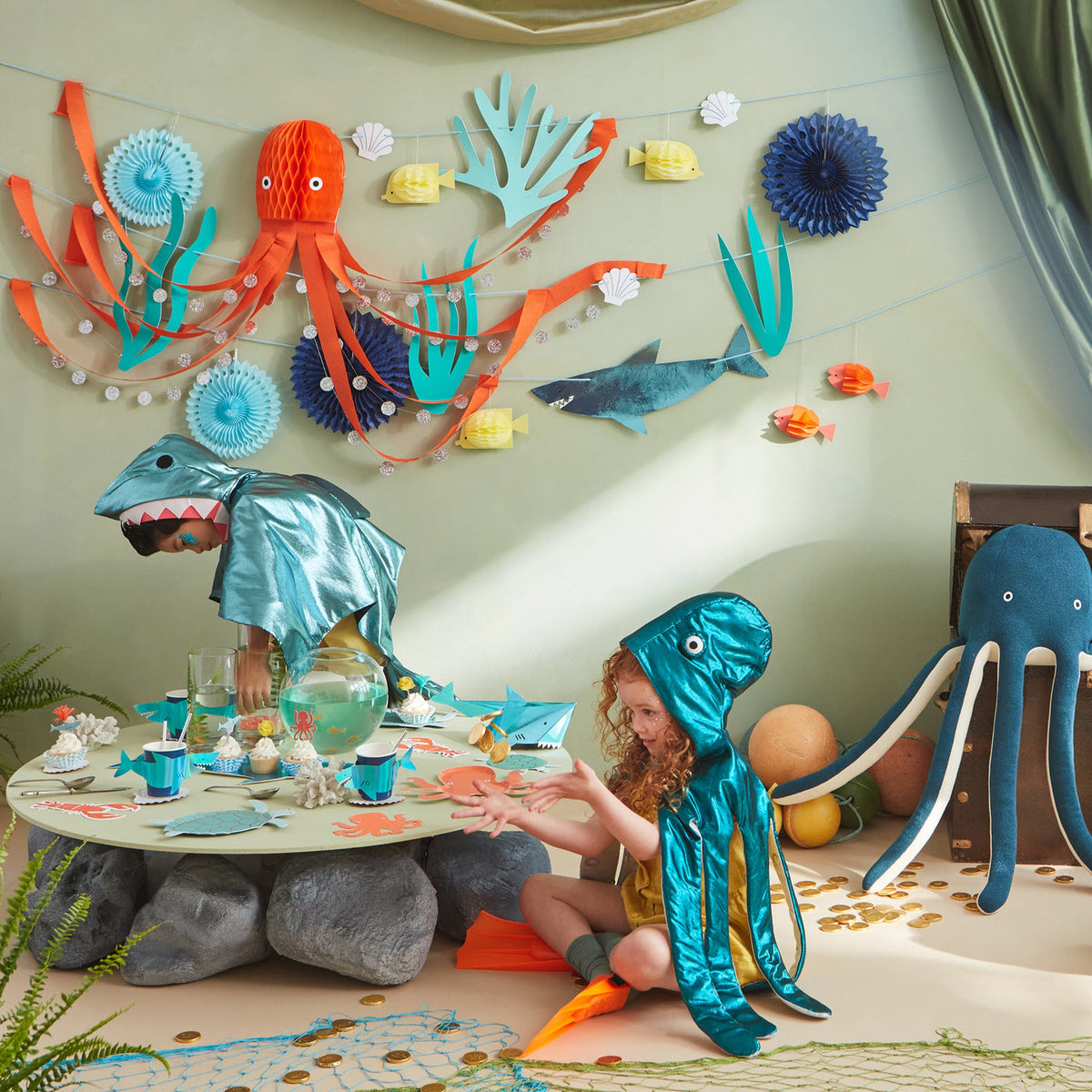 Children in ocean-themed costumes playing at a table with decorative sea creatures on the wall.
