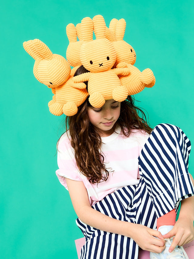 Child wearing a large yellow plush toy on their head against a teal background