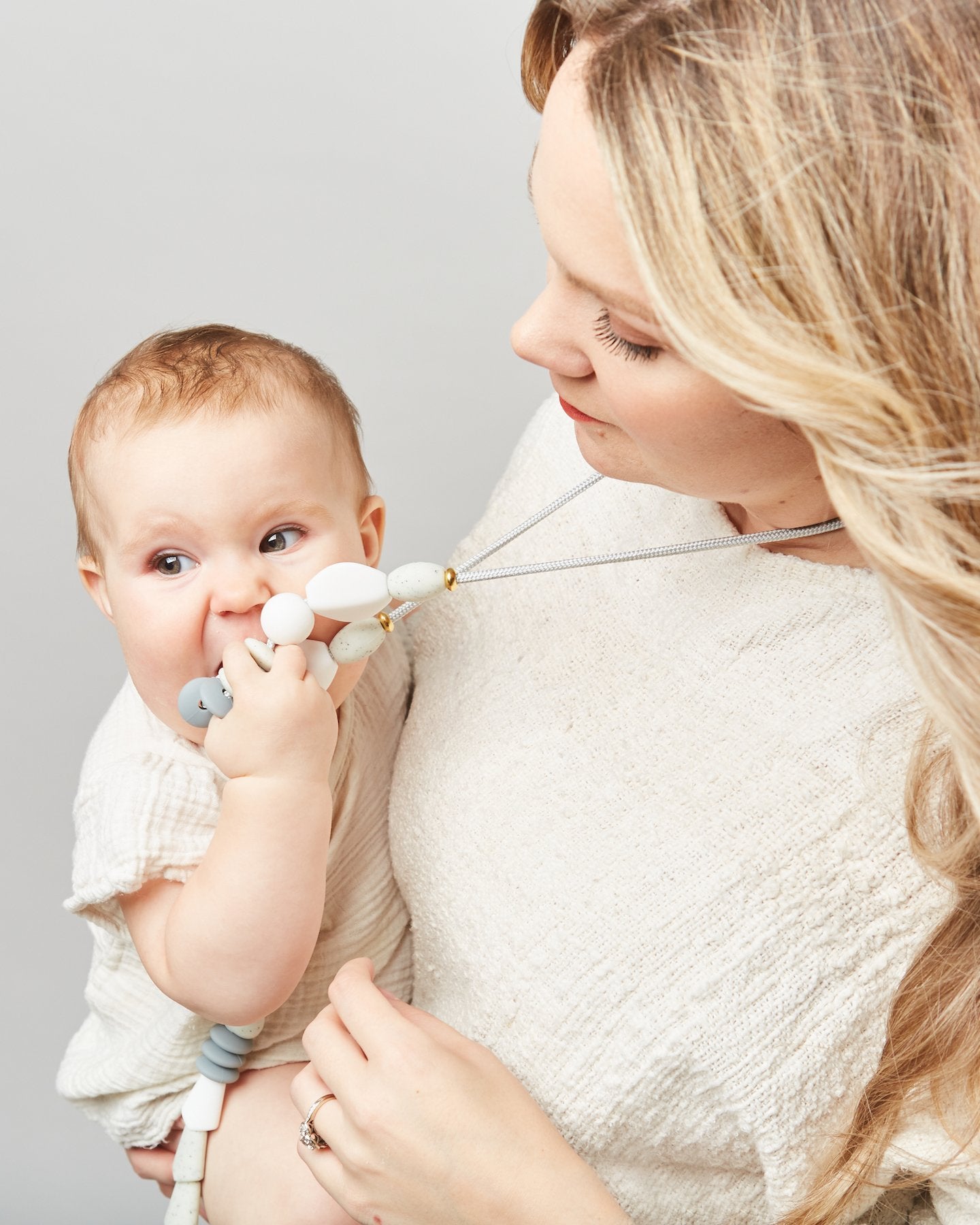 Woman holding a baby with a pacifier against a plain background