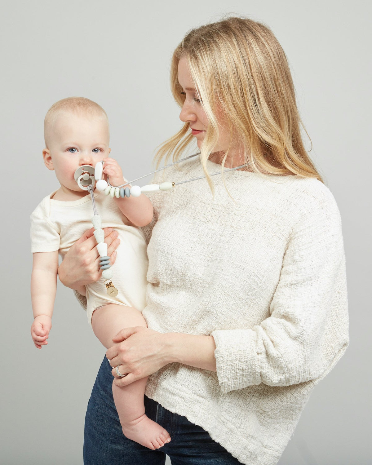 Woman holding a baby with a pacifier against a plain background