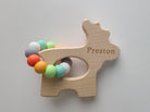 Wooden teething ring with colorful beads and 'Preston' engraving on a light gray background