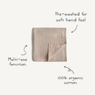 Folded beige towel with text indicating pre-washed feel, multi-use function, and 100% organic cotton on a white background.