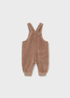 A baby's corduroy overall romper in a warm taupe-brown color, featuring adjustable shoulder straps, a front patch pocket, and ribbed cuffs, shown flat on a light gray background.