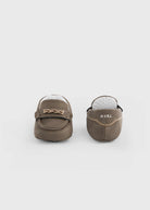 A pair of baby moccasins in taupe brown suede, shown from the back to display the interior. The shoes feature a small decorative bow on the side and the brand name 'M.