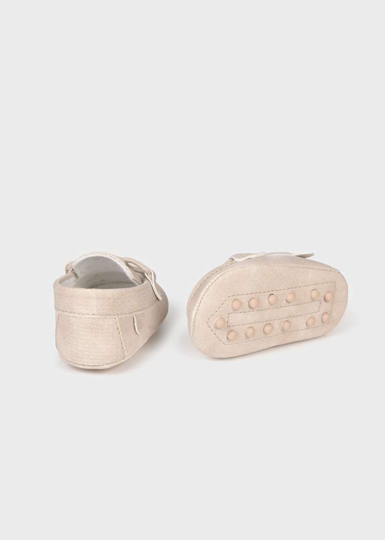 Pair of beige baby shoes with buttons on a light gray background