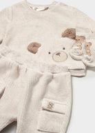 A baby knit two-piece outfit in a soft cream-beige corduroy-like fabric, featuring a long-sleeve top with a teddy bear face applique and matching booties with a teddy bear motif.
