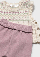 A close-up of a baby knit outfit featuring a cream-colored sleeveless top with a Fair Isle pattern in pink and green, paired with dusty pink knit pants with a buttoned side detail.