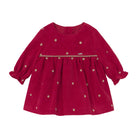 A long-sleeve baby dress in deep magenta corduroy with small beige polka dots and a beige braided trim across the chest, shown flat on a white background.