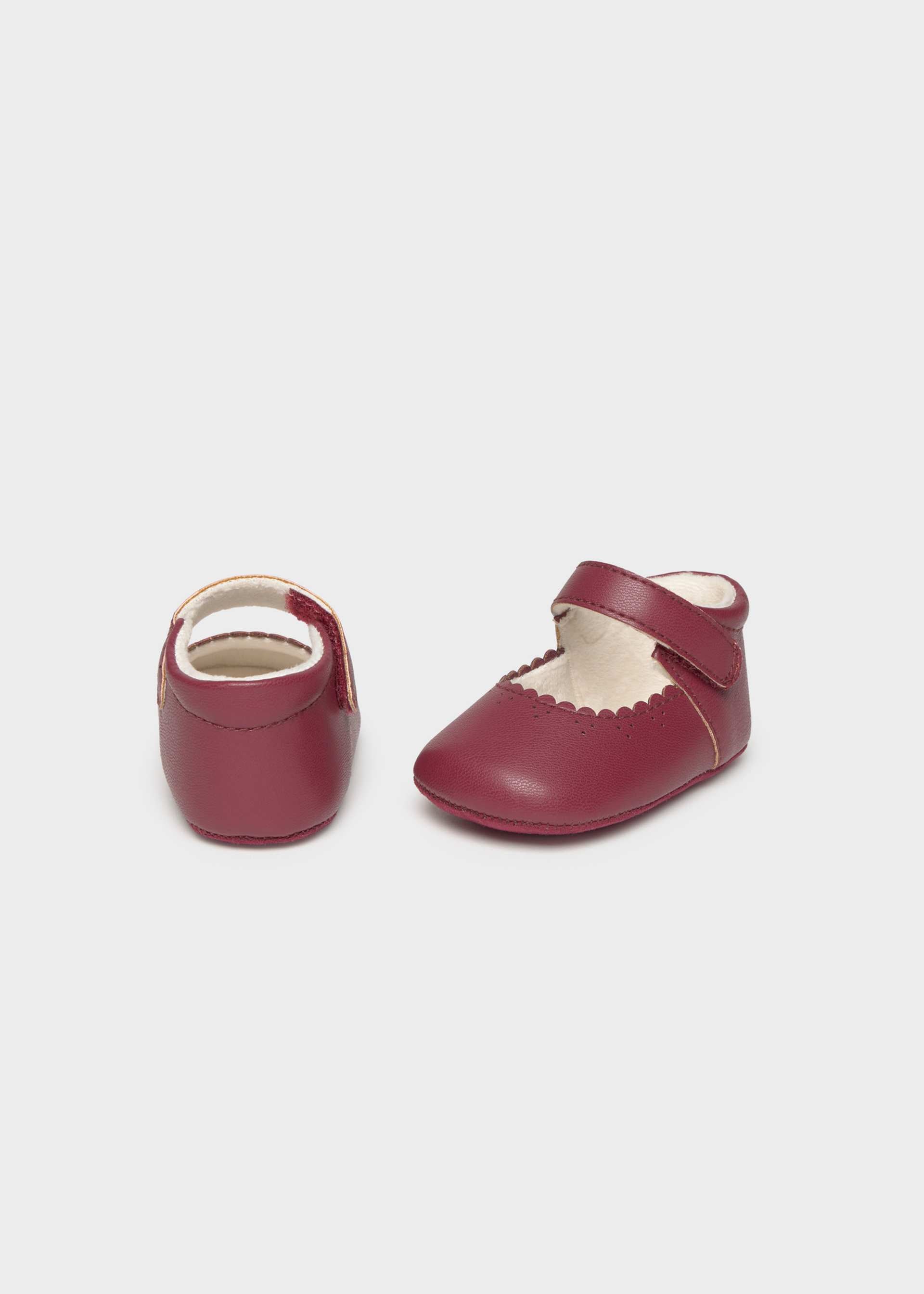 Pair of maroon baby shoes with white soles on a light gray background