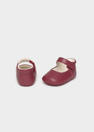 Pair of maroon baby shoes with white soles on a light gray background