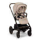 A profile view of a MIXX Next + Pipa Aire RX Travel System by Nuna stroller in Biscotti featuring a beige seat and canopy, a black frame, and a brown leatherette handlebar and armbar, set against a clean white background.