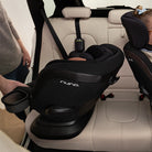 Nuna car seat being installed in a vehicle with a person assisting.