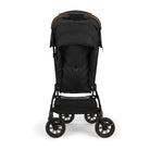Nuna TRVL 360 lightweight travel stroller in Caviar black, shown in a three-quarters rear view against a clean white background. The stroller features a black sun canopy, a brown leatherette pushbar, an under-seat storage basket, and 360-degree swivel wheels.