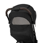 Nuna TRVL 360 lightweight travel stroller in Caviar black, shown from the rear with the canopy extended to reveal a mesh ventilation window and a brown leatherette pushbar against a clean white background.
