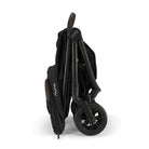 Nuna TRVL 360 lightweight travel stroller in Caviar black, shown in a folded, freestanding position against a clean white background with a brown leatherette pushbar visible at the top.